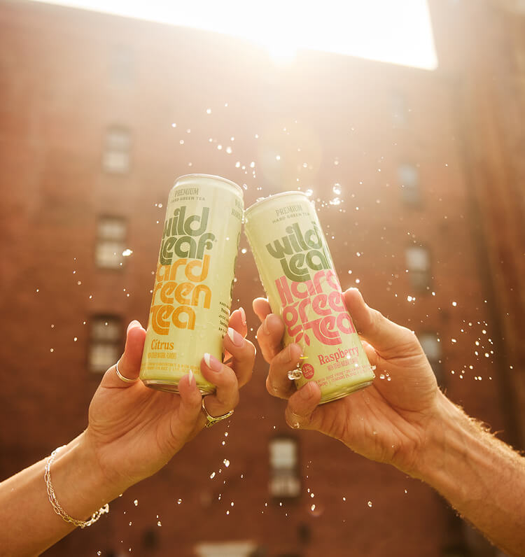 Two people cheersing with cans of Wild Leaf Hard Green Tea